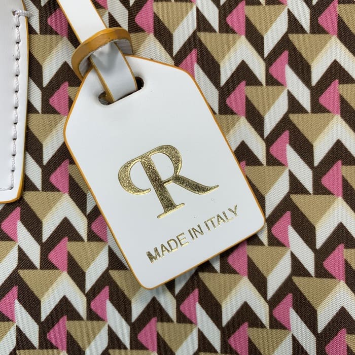 Een close-up van een wit Roberta Pieri-bagagelabel met de letters "R" in goud en de woorden "MADE IN ITALY" bevestigd aan een mini-plunjezak met bruine, beige en roze geometrische patronen.